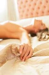 Nude woman gripping sheets on bed stock photo